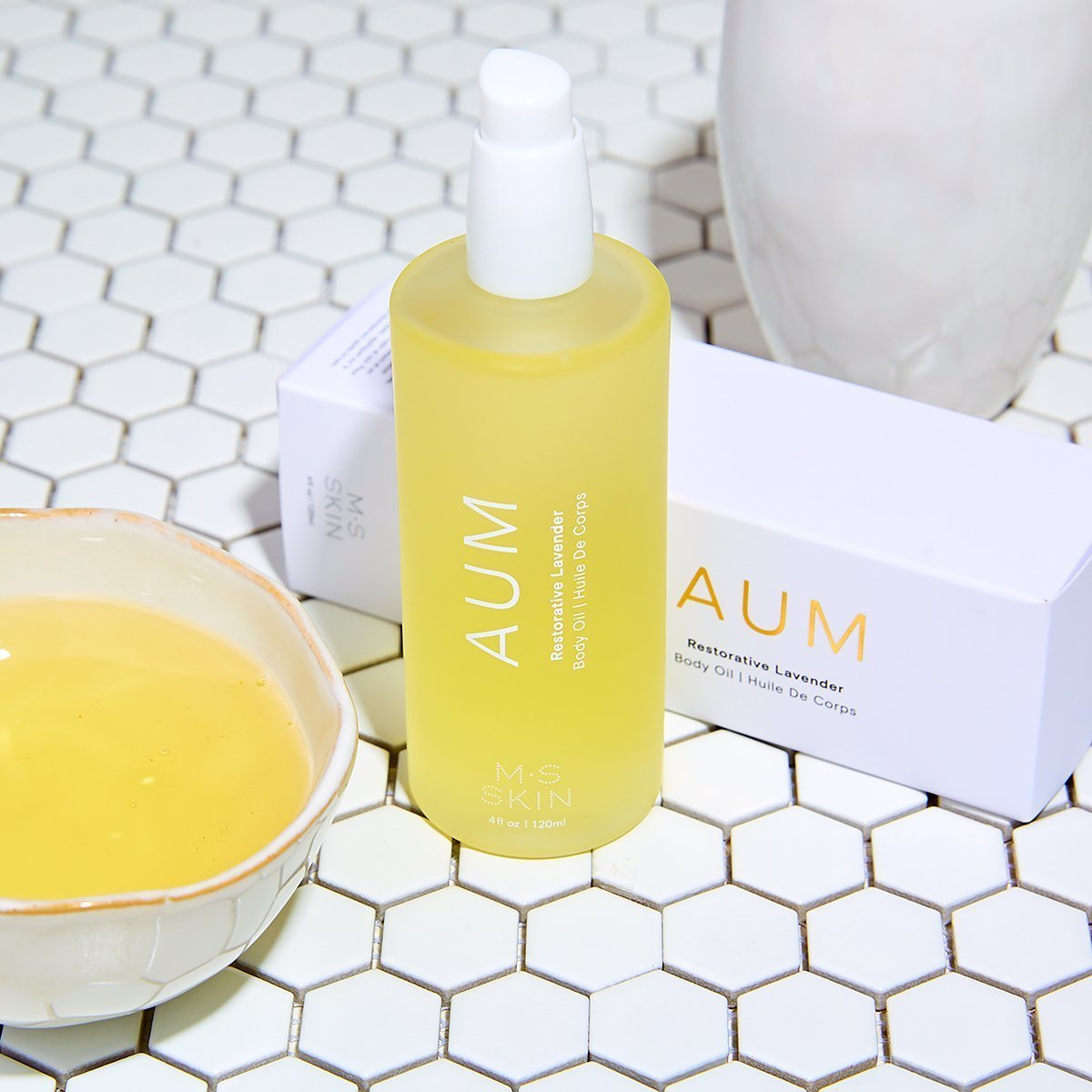 M.S Skincare AUM Lavender Restorative Body Oil -luxury skincare in a white bottle on a tile background with a bowl of oil.