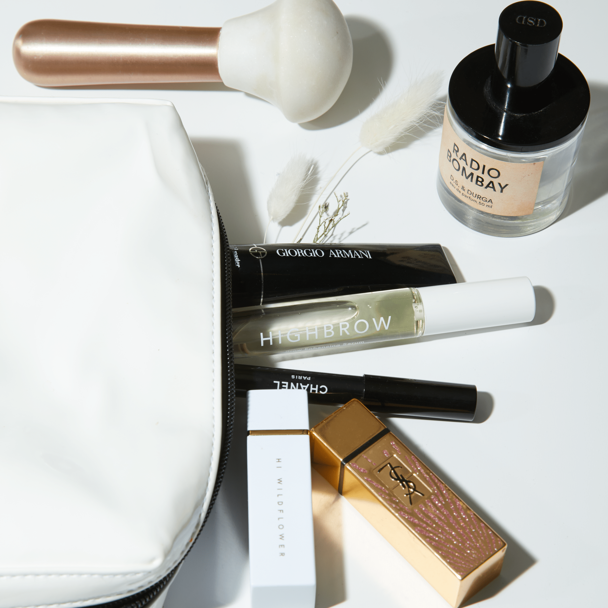 M.S Skincare HIGHBROW Brow Enhancing Serum spilling out a white vinyl Violet grey makeup bag with other luxury brands.